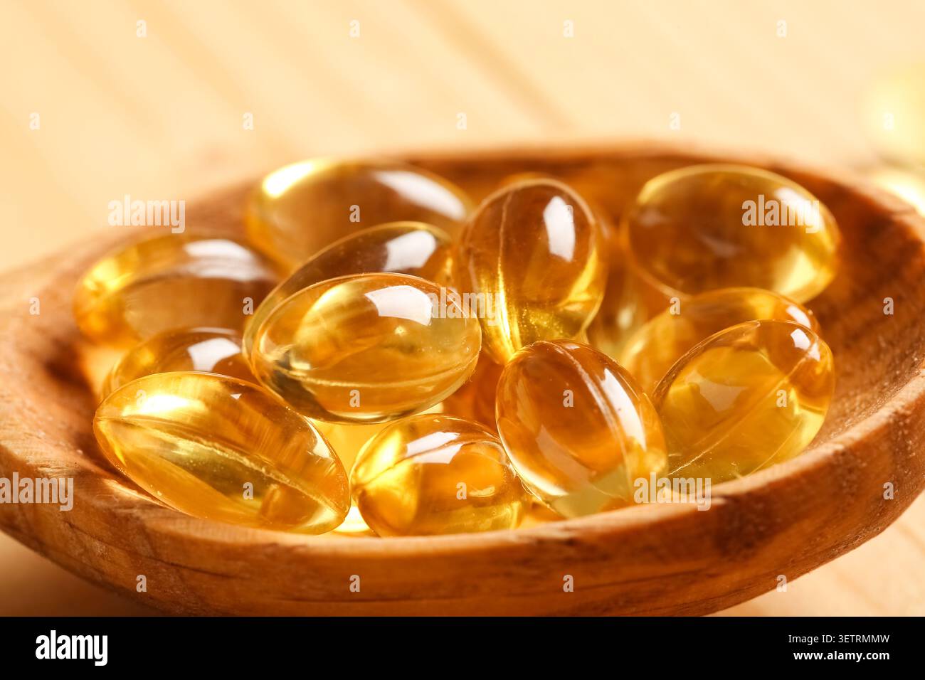 Gros plan de capsules de gel souple jaunes dans une cuillère en bois Banque D'Images