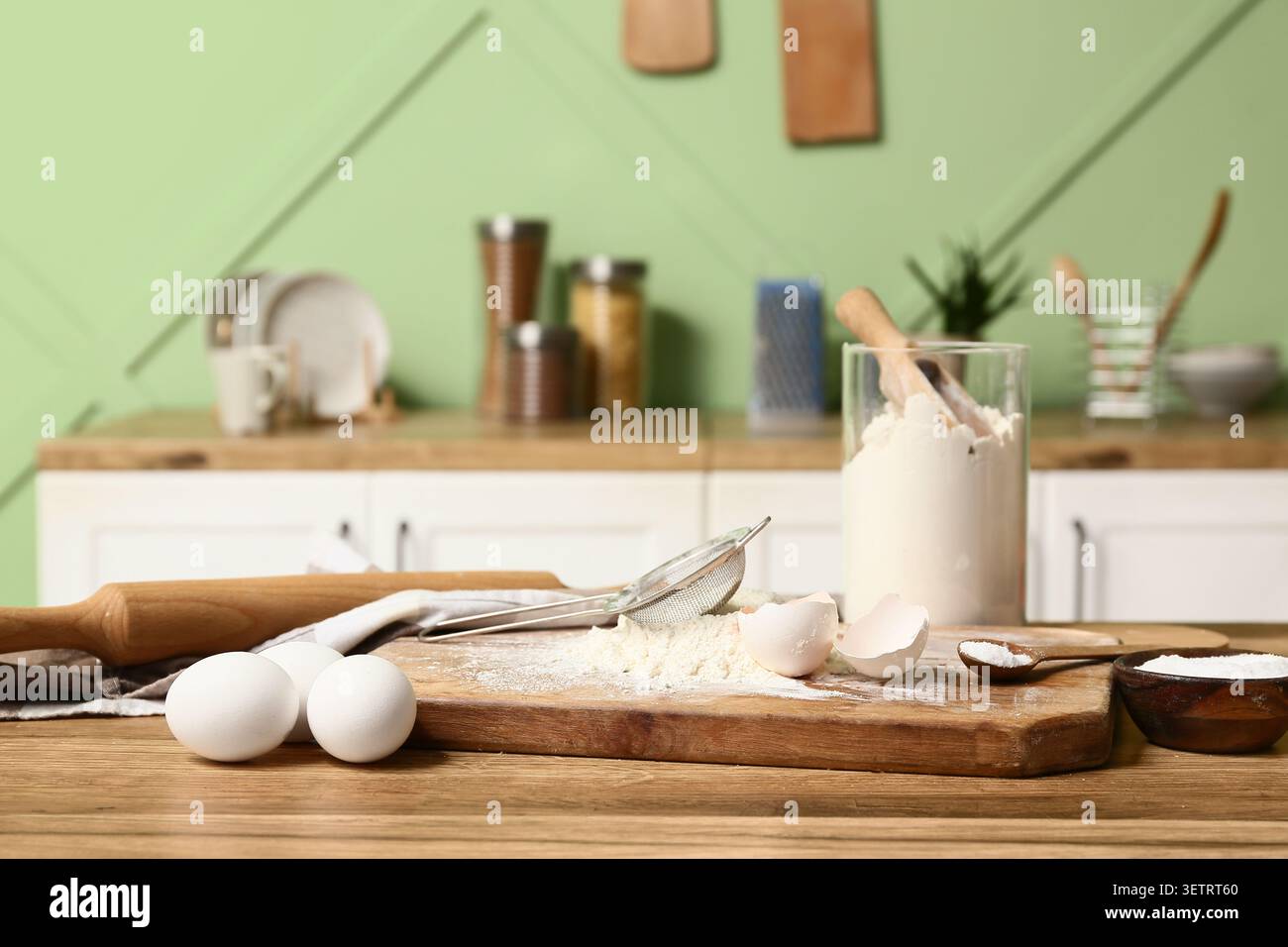 Planche à découper avec de la farine, des œufs, du bicarbonate de soude et des ustensiles de cuisine pour préparer la pâte sur une table en bois dans la cuisine Banque D'Images