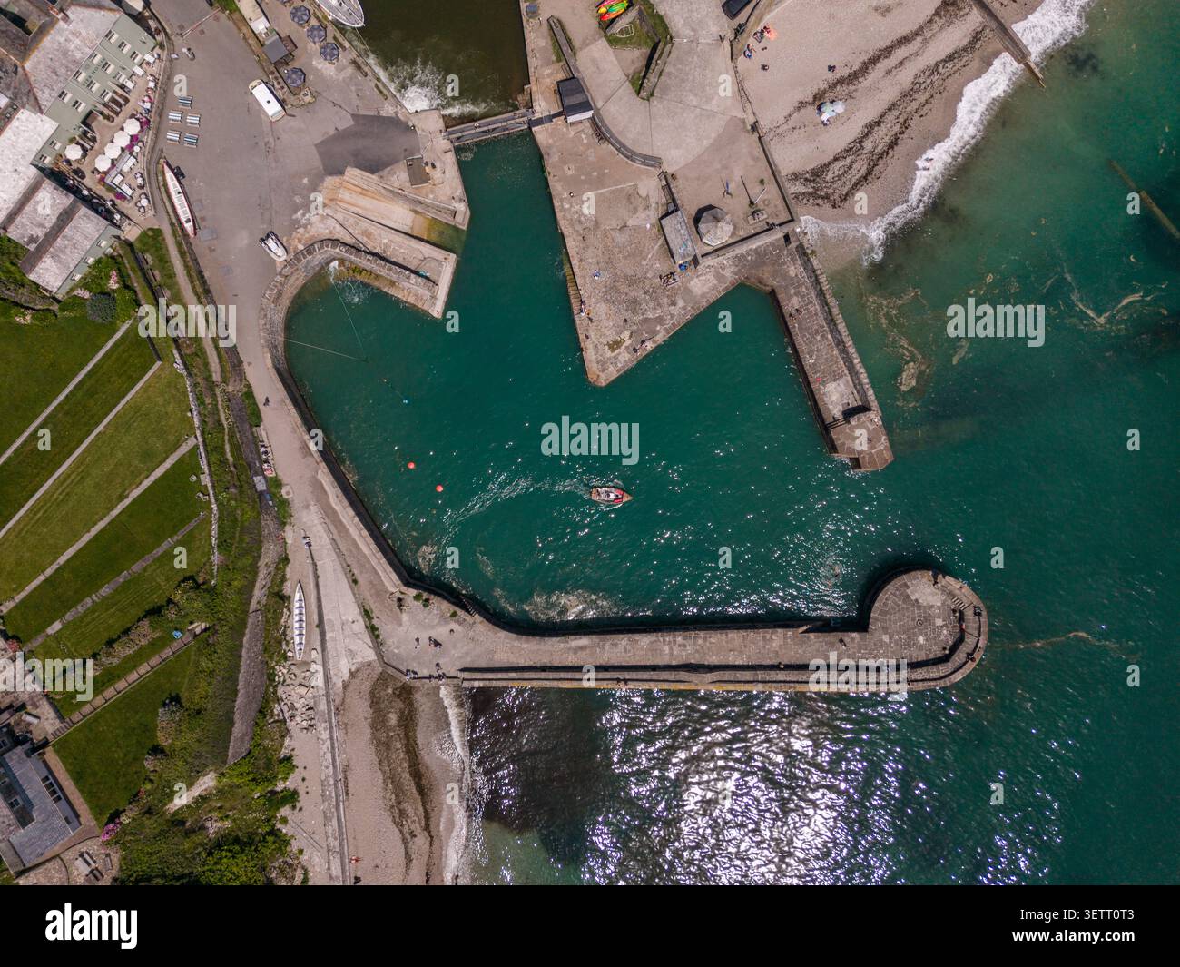 Vue aérienne de haut en bas de la jetée historique du port de Charlestown et de la mer turquoise avec un seul petit bateau naviguant dans la zone d'eau protégée de Cornwa Banque D'Images