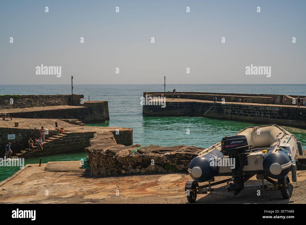 Un canot gonflable sur une petite remorque repose sur le quai de pierre brute dans le port historique de Charlestown, surplombant la mer turquoise calme Banque D'Images