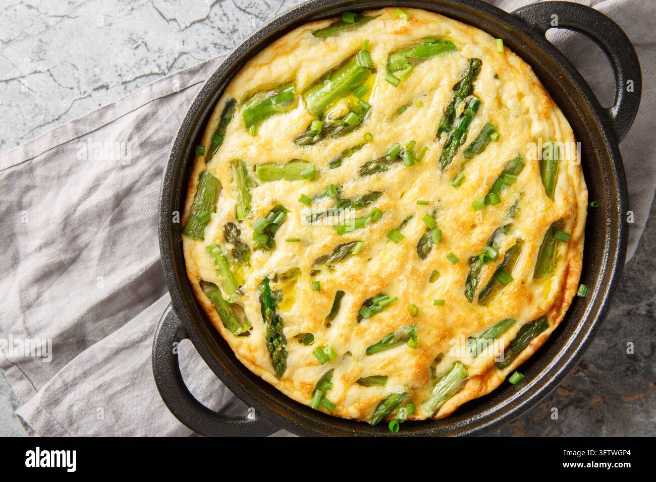 Délicieuse frittata d'asperges vertes aux herbes fraîches en gros plan dans la poêle sur la table. Vue horizontale de dessus Banque D'Images