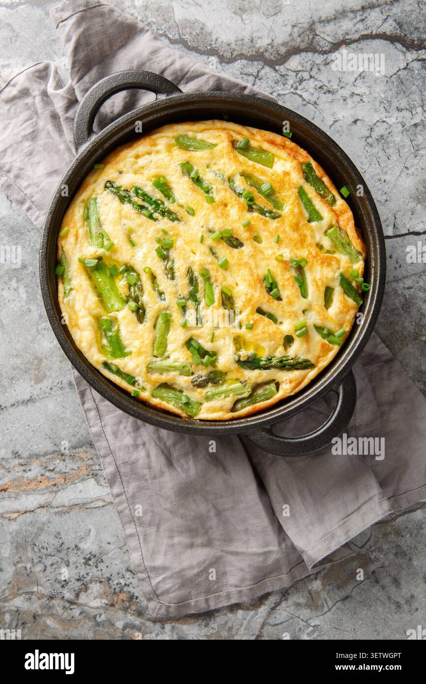 Frittata savoureux cuit au four avec des asperges et une herbe fraîche en gros plan dans la poêle sur la table. Vue de dessus verticale Banque D'Images
