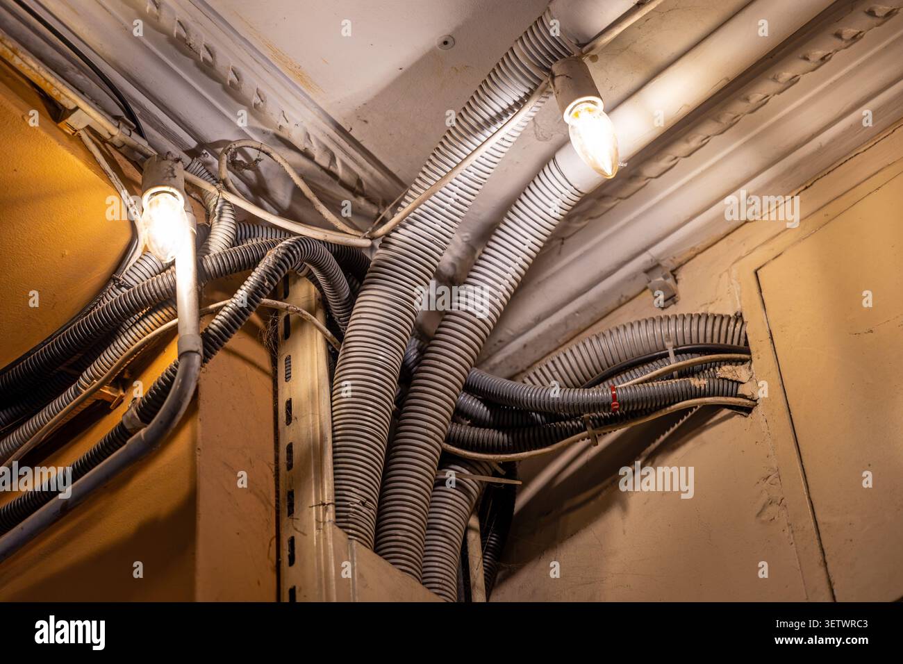 Conduits électriques et ampoules exposés dans le coin du plafond. Coin de plafond avec conduits électriques ondulés exposés, câbles, tuyaux et ampoules incandescentes Banque D'Images