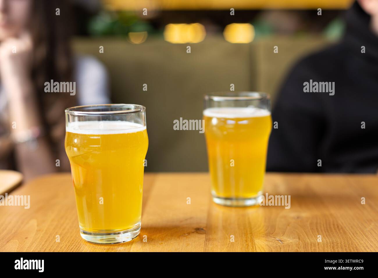 Deux verres de bière brumeuse sur la table en bois. Deux verres de bière brumeuse dorée avec dessus mousseux assis sur une table en bois dans un cadre de bar légèrement flou avec Banque D'Images