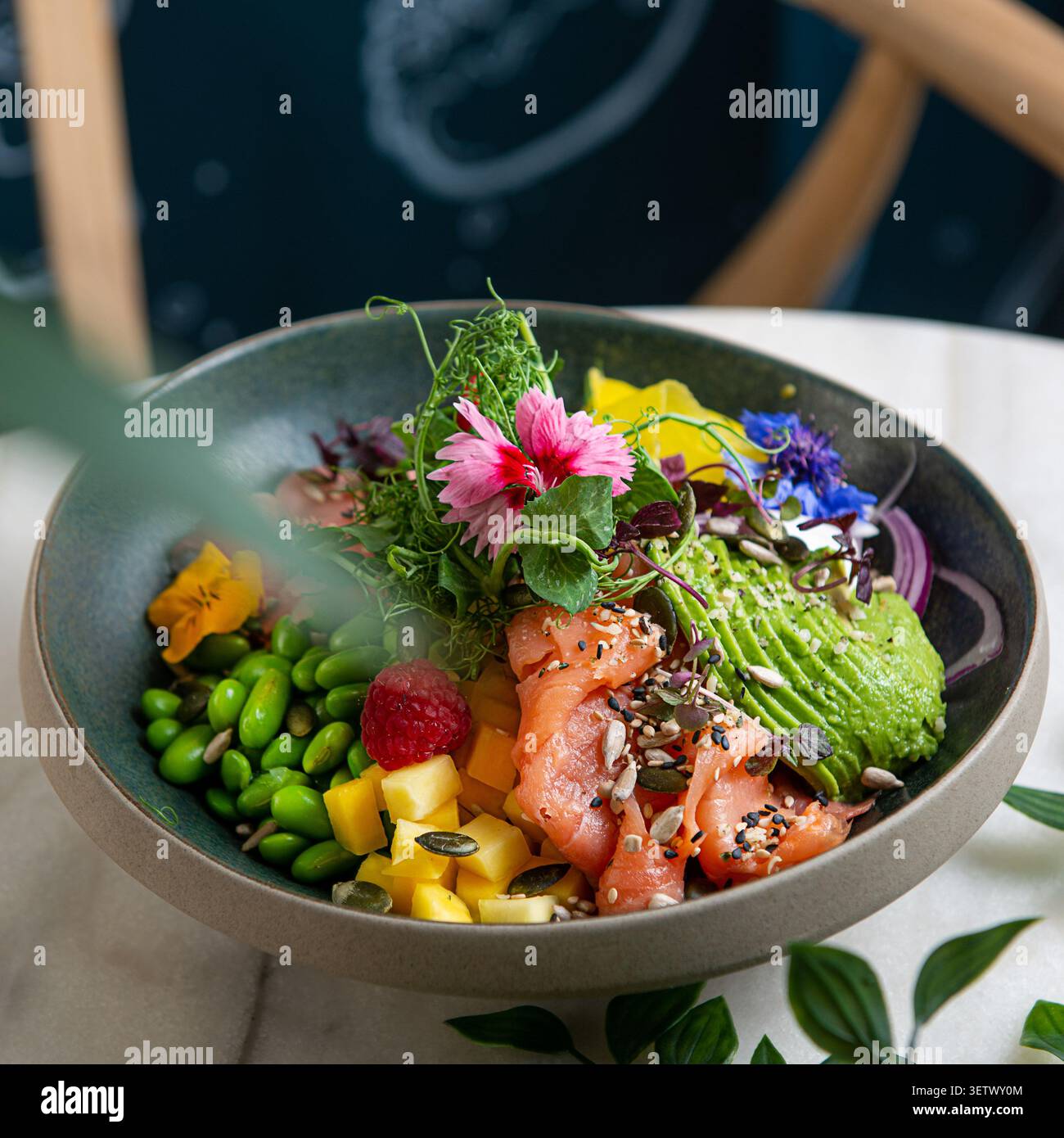 Bol à saumon vibrant avec avocat, mangue, edamame et fleurs comestibles. Banque D'Images