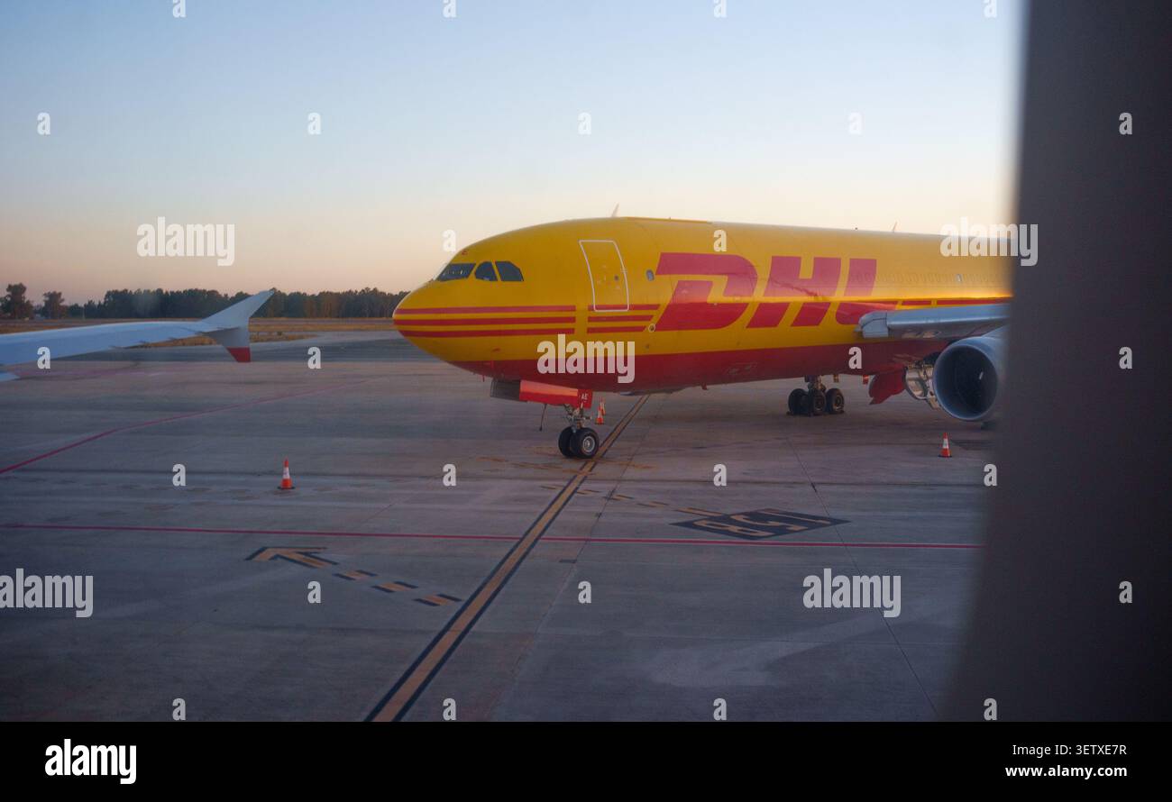 Un avion DHL sur la piste d'un aéroport international vu par la fenêtre au coucher du soleil Banque D'Images