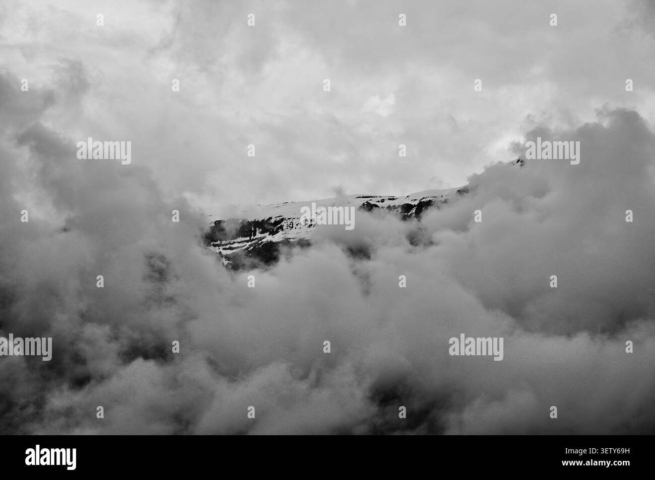 Un paysage horizontal noir et blanc spectaculaire mettant en valeur un sommet de montagne de haute altitude des Alpes Dolomites entouré d'un épais brouillard roulant. Banque D'Images