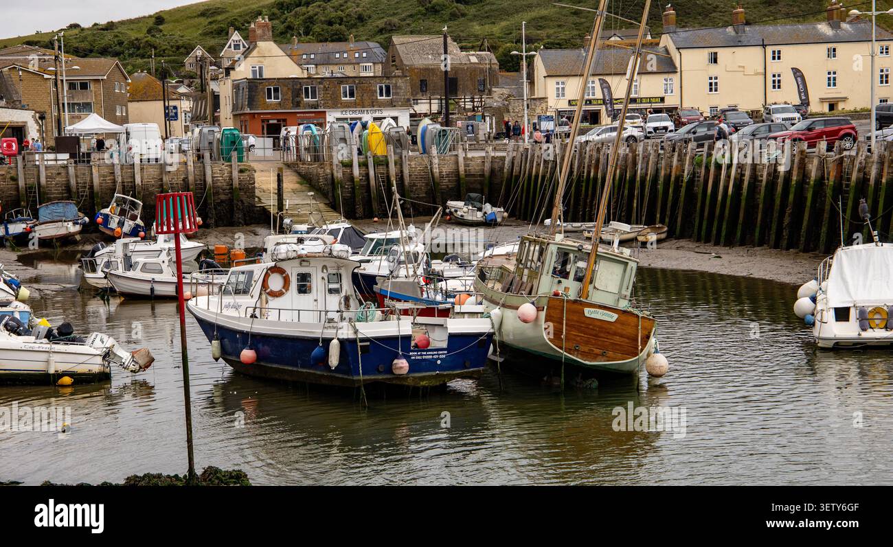Bateaux de pêche amarrés à marée basse dans un port pittoresque avec un village pittoresque en toile de fond West Bay Dorset UK Banque D'Images