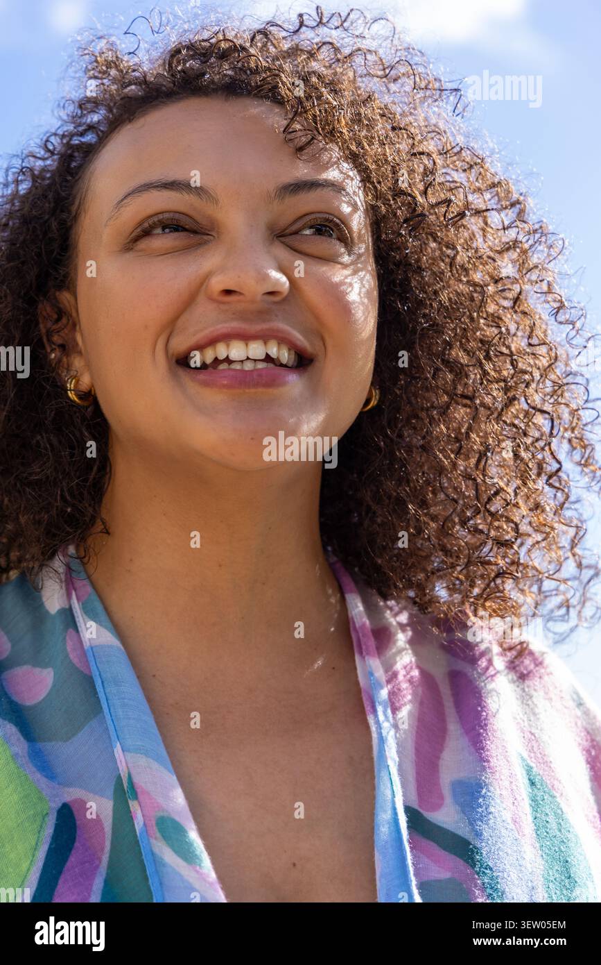 Femme afro-américaine souriante et regardant vers le ciel à l'extérieur, portant châle coloré et cerceaux en or Banque D'Images