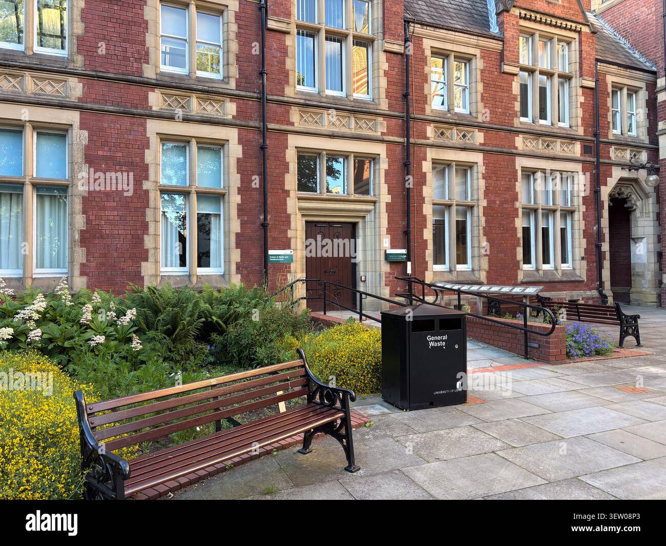 Bâtiment universitaire historique en brique rouge avec garniture en pierre à Leeds, Royaume-Uni, avec un banc de parc en bois et une poubelle générale au premier plan. Banque D'Images