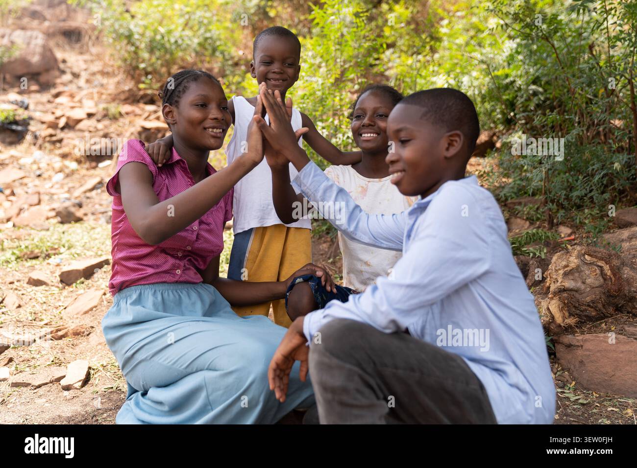 Dans la lumière chaude sous l'arbre, les frères et sœurs africains rient et se mettent à cinq, capturant l'énergie d'une enfance heureuse et la beauté de f Banque D'Images