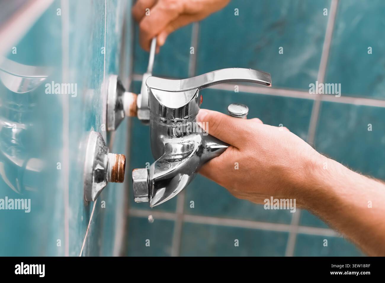 Homme enlevant un vieux robinet qui fuit avec un tournevis, exposant les tuyaux rouillés - réparation de plomberie bricolage et rénovation de salle de bains par un bricoleur. Hig Banque D'Images