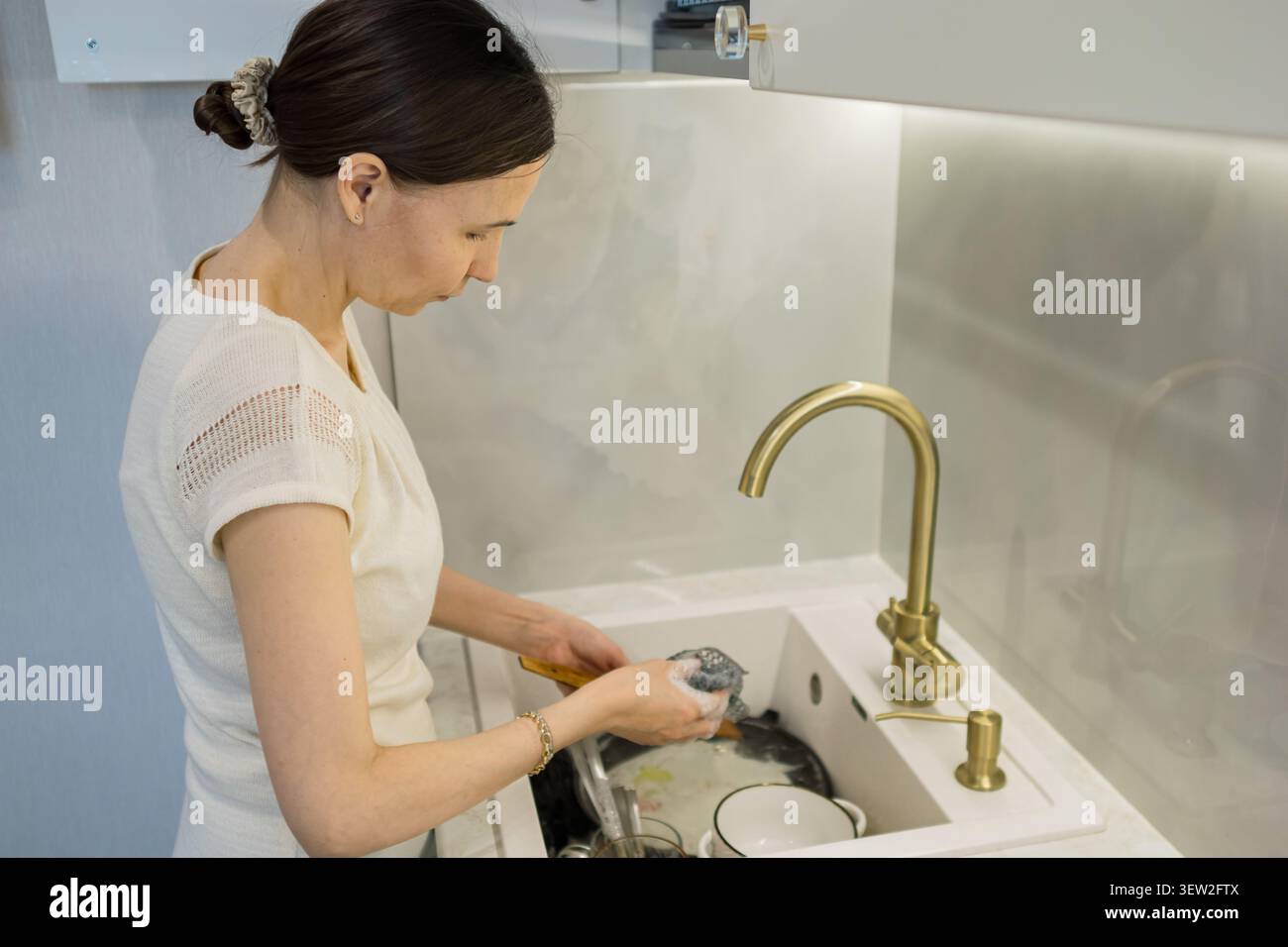 Jeune femme lavant la vaisselle dans un évier de cuisine moderne Banque D'Images