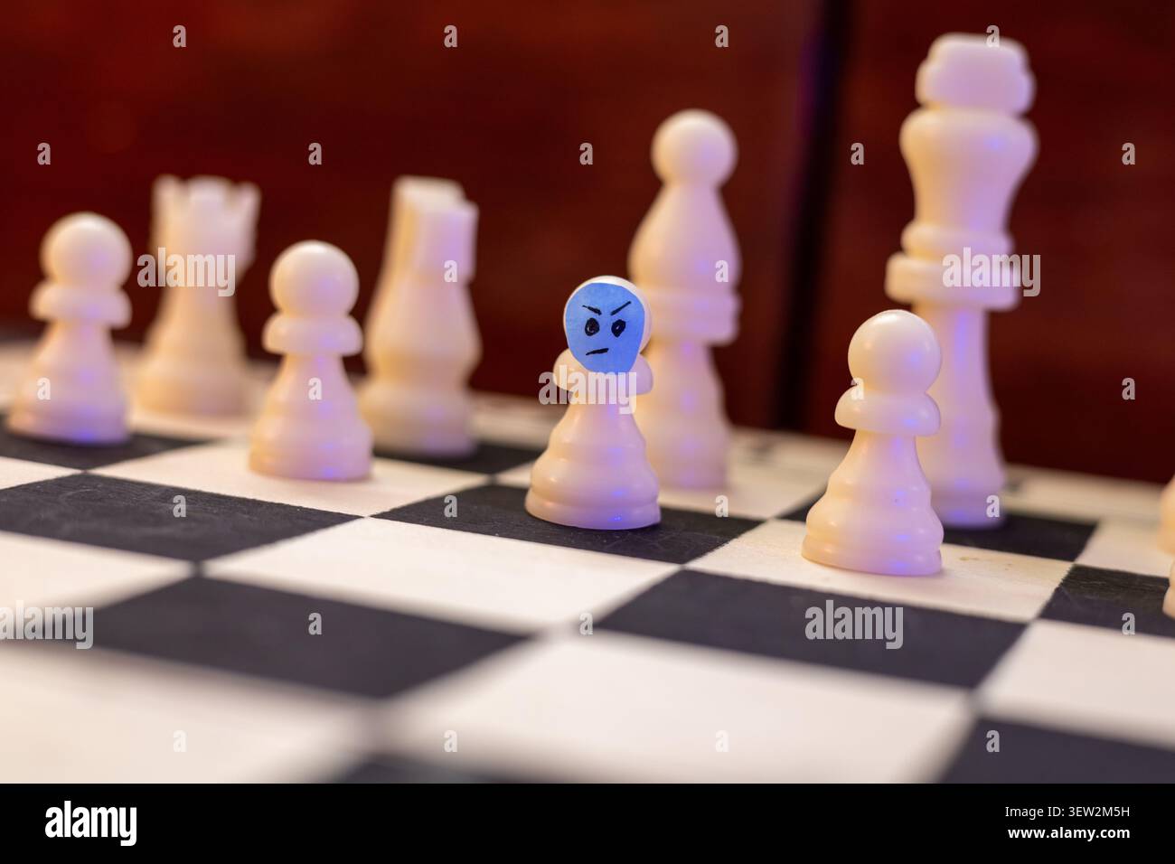 Pion d'échecs blanc en colère debout parmi d'autres pièces sur échiquier Banque D'Images
