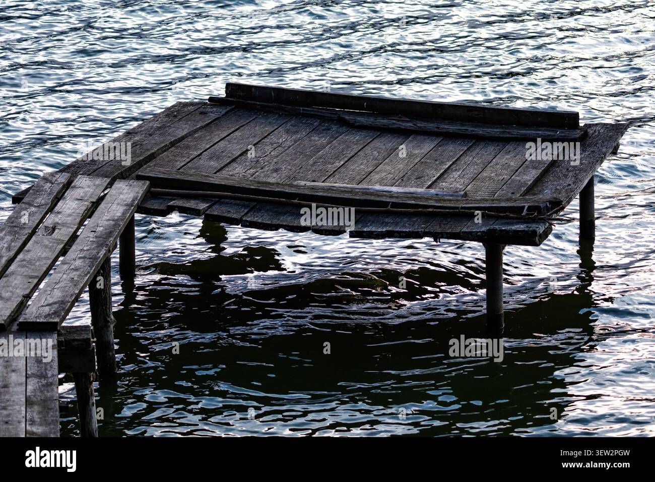 Vieille plate-forme en bois se trouve juste au-dessus de la surface du lac relié à une passerelle étroite comme les vagues texturées reflètent le ciel suggérant un rustique paisible Banque D'Images