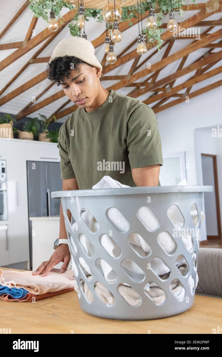 Homme pliant le linge sur la table en bois dans la cuisine de la ferme avec panier à linge en plastique gris Banque D'Images