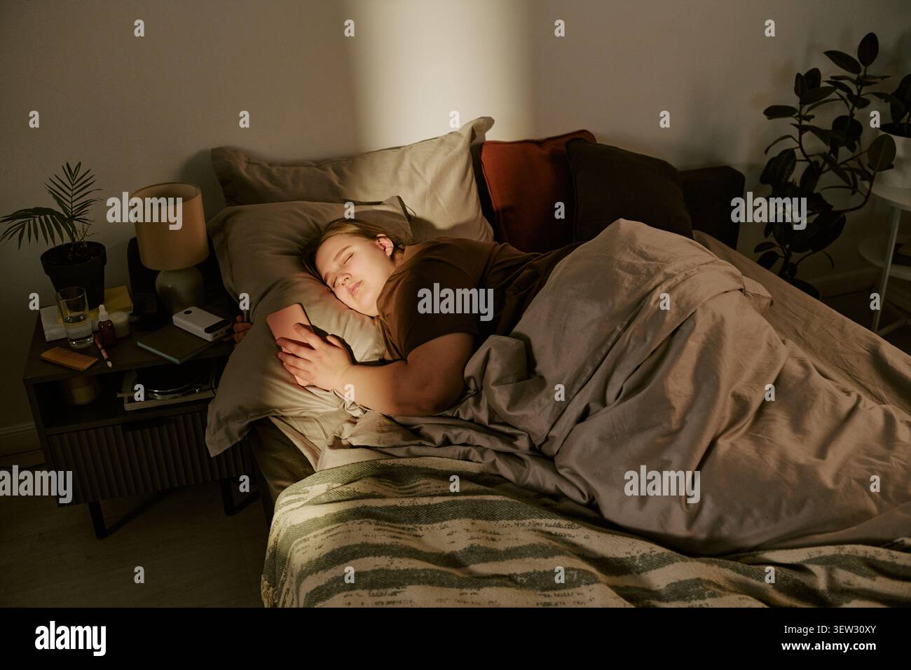 Femme de taille plus dormant tout en tenant smartphone dans le lit la nuit Banque D'Images