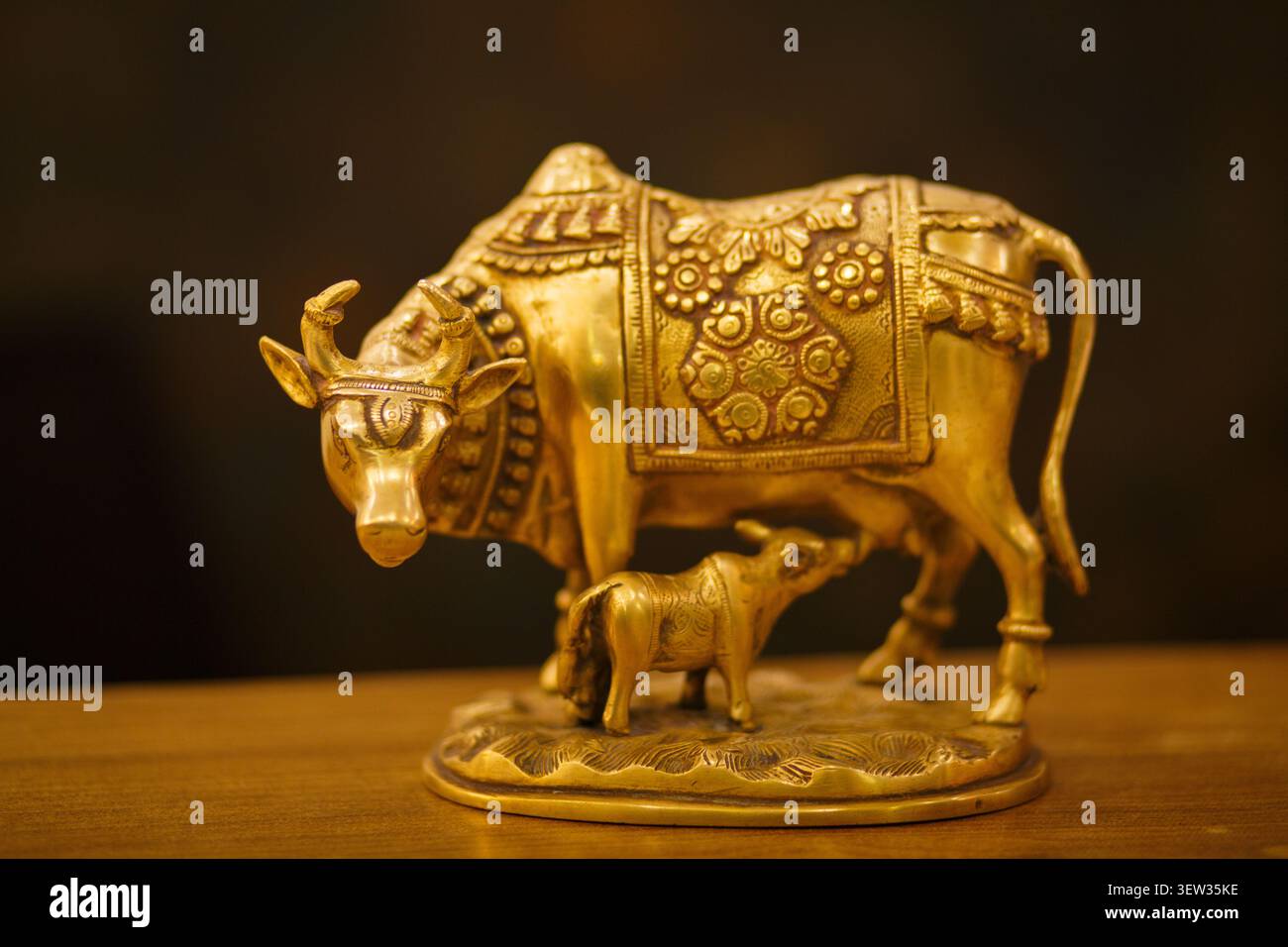 Figurine en laiton de vache et veau dorée sur surface en bois avec fond sombre Banque D'Images