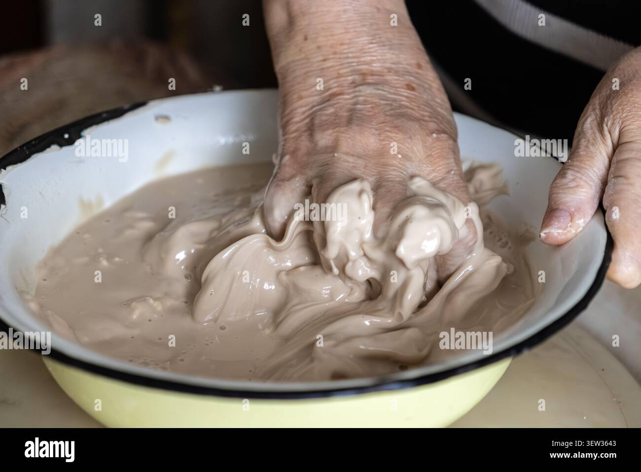 Mains matures mélangeant un mélange de farine fermentée et d'eau dans un vieux bassin, représentant la patience et l'artisanat authentique derrière le levain à la main bre Banque D'Images