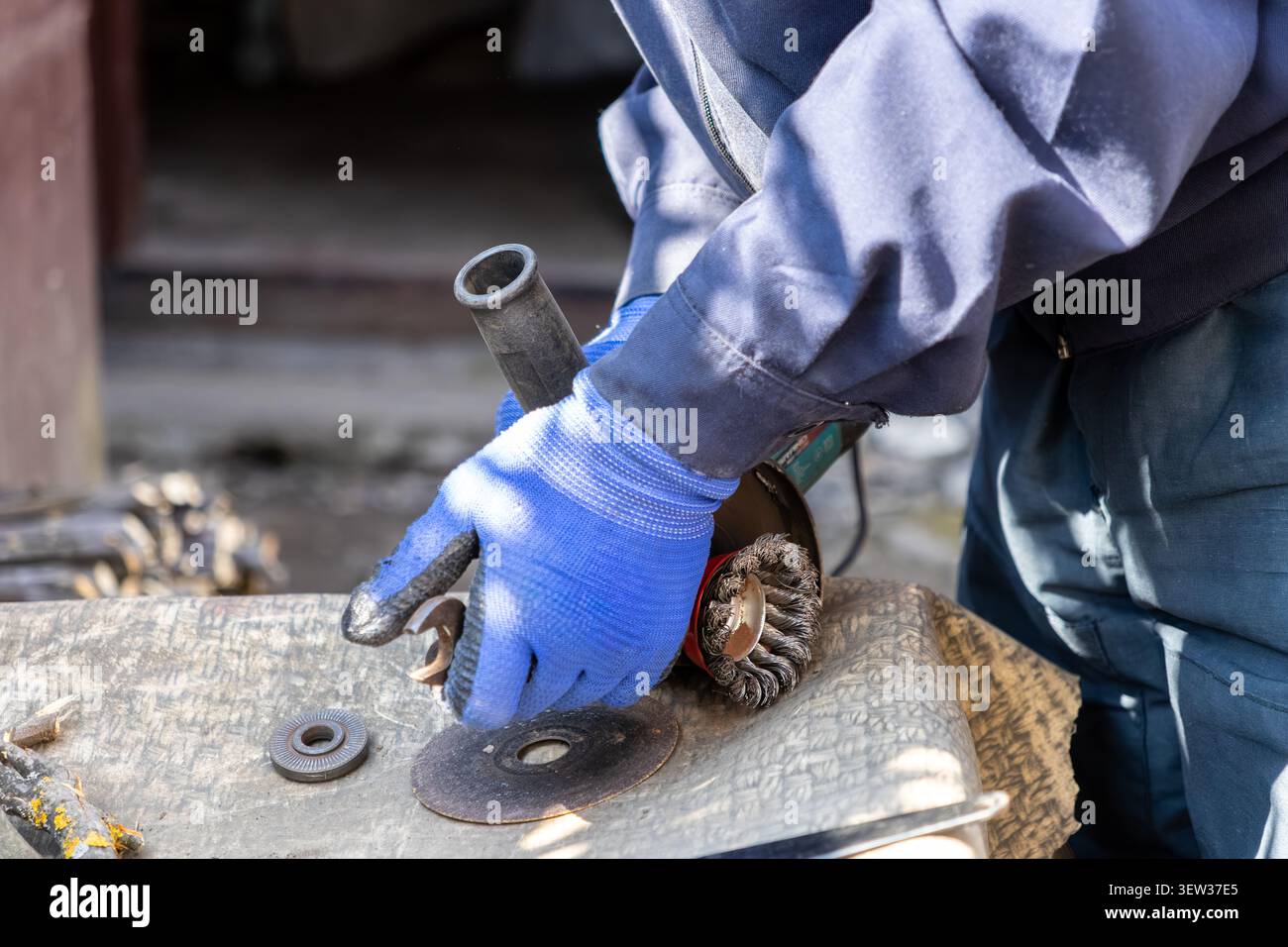 Un technicien qualifié portant des gants de protection bleus nettoie les composants métalliques avec une brosse métallique de meuleuse d'angle, illustrant l'expertise de précision en métallurgie Banque D'Images