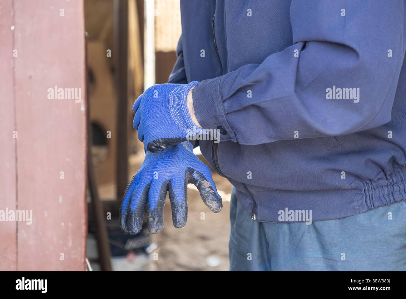 Une personne portant un équipement de protection tire sur des gants bleus pour commencer le travail physique sur un site industriel, illustrant l'accent mis sur la préparation des tâches et Banque D'Images
