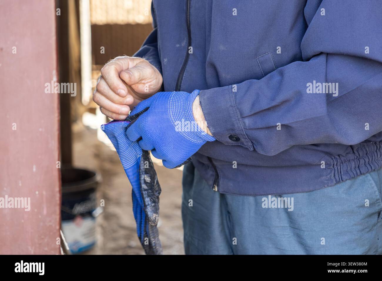 Un ouvrier manuel ajuste des gants de travail bleus résistants pour se préparer en toute sécurité aux travaux de construction ou d'entretien, illustrant l'importance du GE personnel Banque D'Images