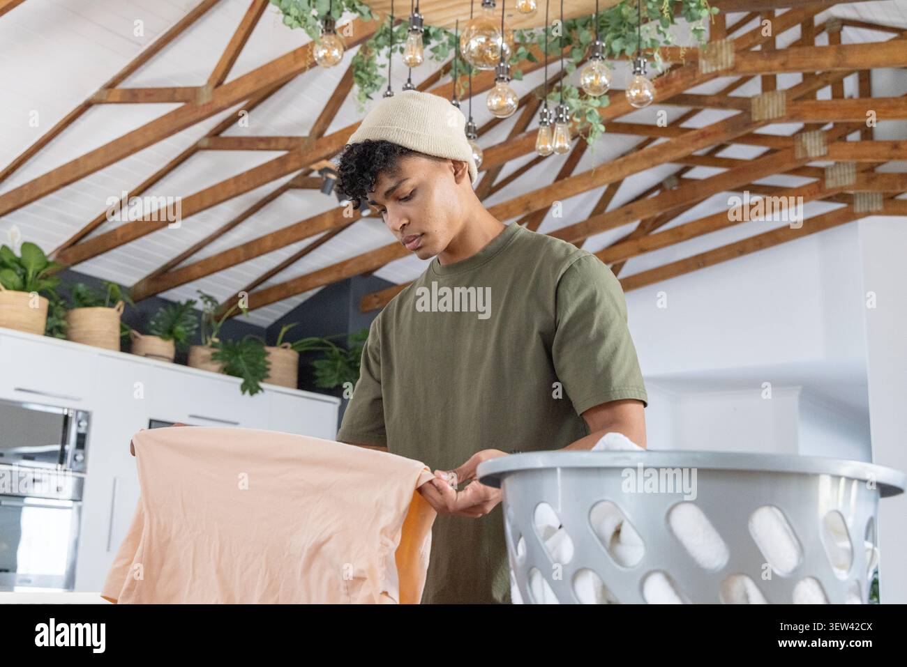 Homme africain au début des années 20 pliant la chemise de pêche sur le panier à linge gris dans la cuisine de la ferme Banque D'Images
