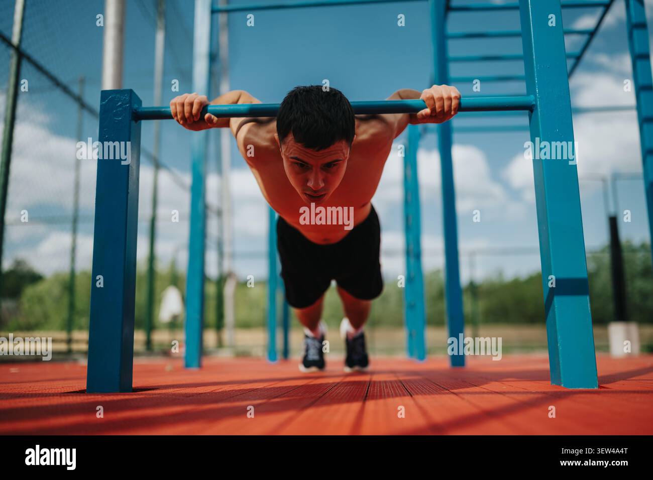 Homme sportif effectuant un push-up incliné sur des barres calisthenics extérieures pendant l'entraînement de jour Banque D'Images