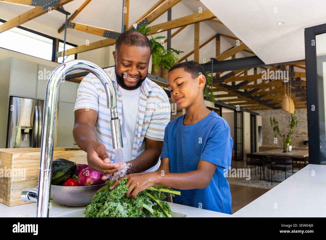 Père afro-américain et fils adolescent lavant le chou frisé à l'évier sous le robinet avec passoire Banque D'Images