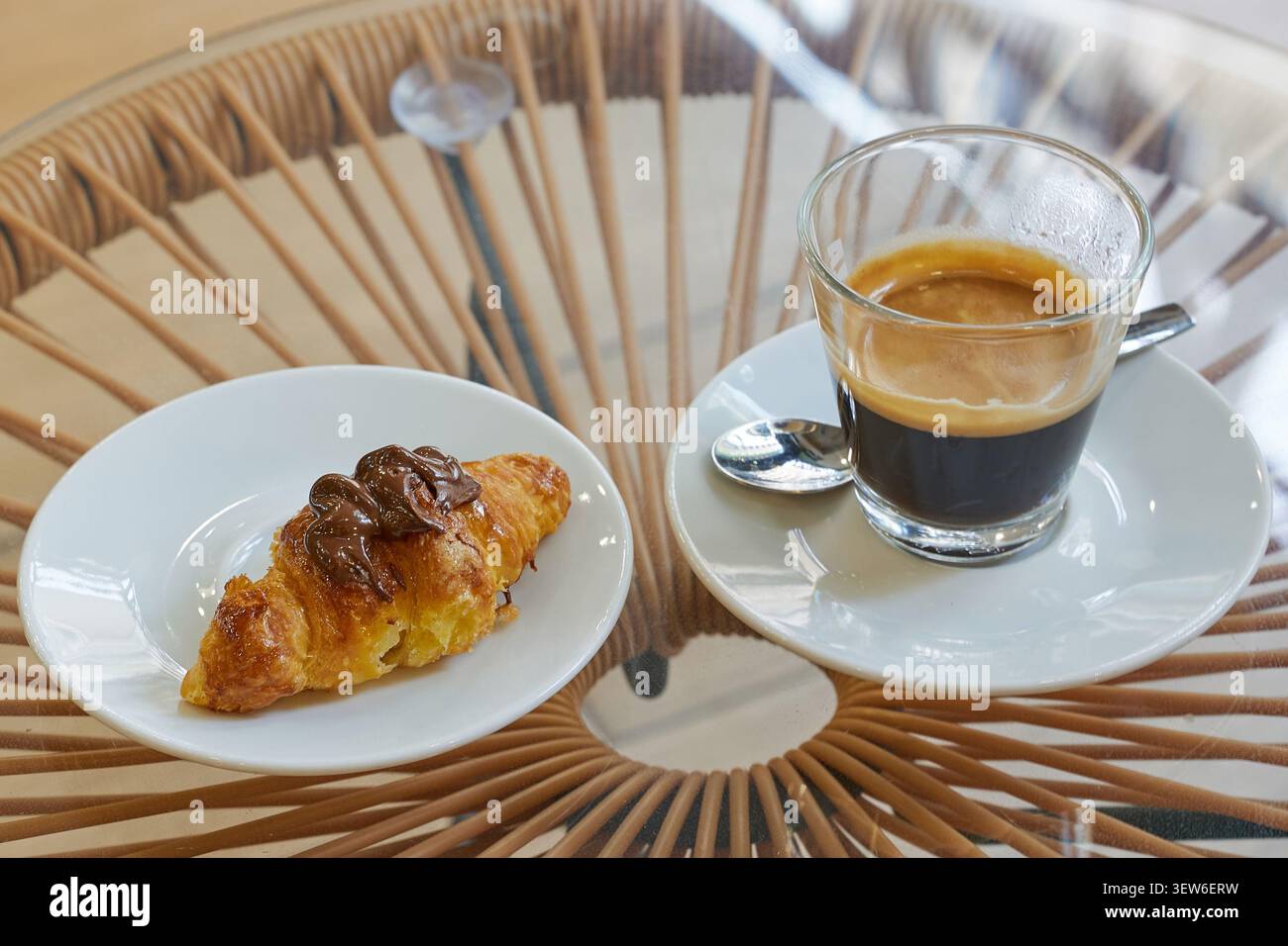 Café expresso et un petit croissant au chocolat sur une table en verre dans un café Banque D'Images