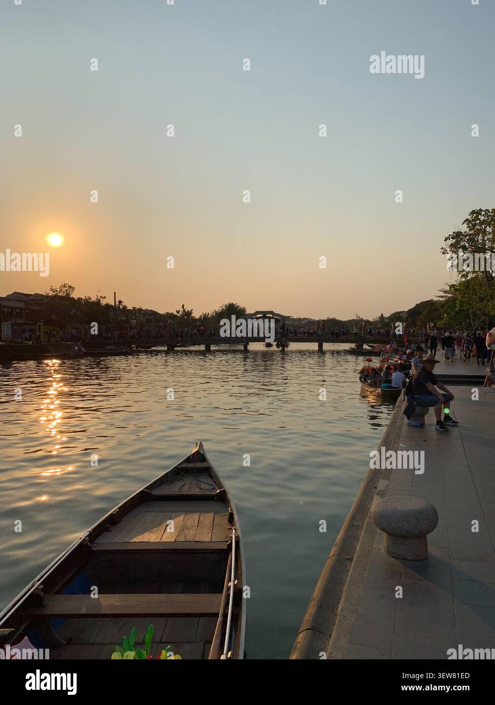 Un coucher de soleil doré sur la rivière Thu bon dans la ville antique de Hoi an, Vietnam, avec un bateau traditionnel en bois au premier plan et les habitants se sont rassemblés le long du - Image de stock capturée avec un smartphone