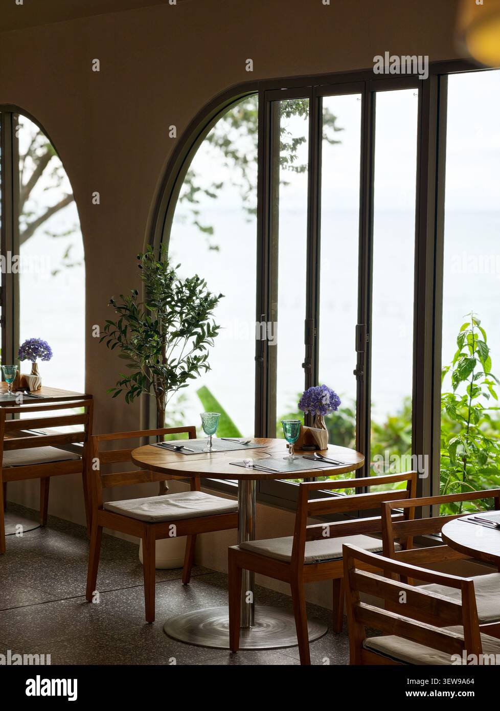 Intérieur élégant du café avec mobilier en bois, lumière naturelle douce et vue paisible sur le jardin à travers de grandes fenêtres cintrées. Banque D'Images