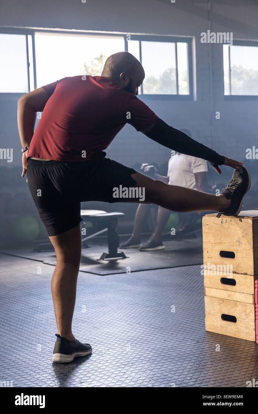 Divers hommes de gymnastique étirant la jambe droite sur des boîtes en bois empilées en plyo à la salle de gym, regardez visible Banque D'Images