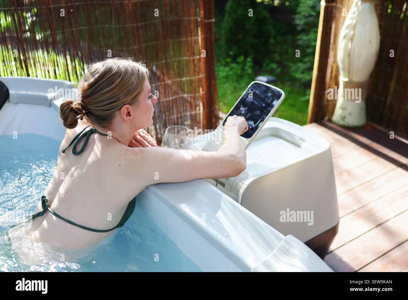 Femme profitant d'un bain relaxant dans un bain à remous extérieur moderne tout en ajustant les commandes intelligentes, alliant bien-être, confort et technologie. Banque D'Images