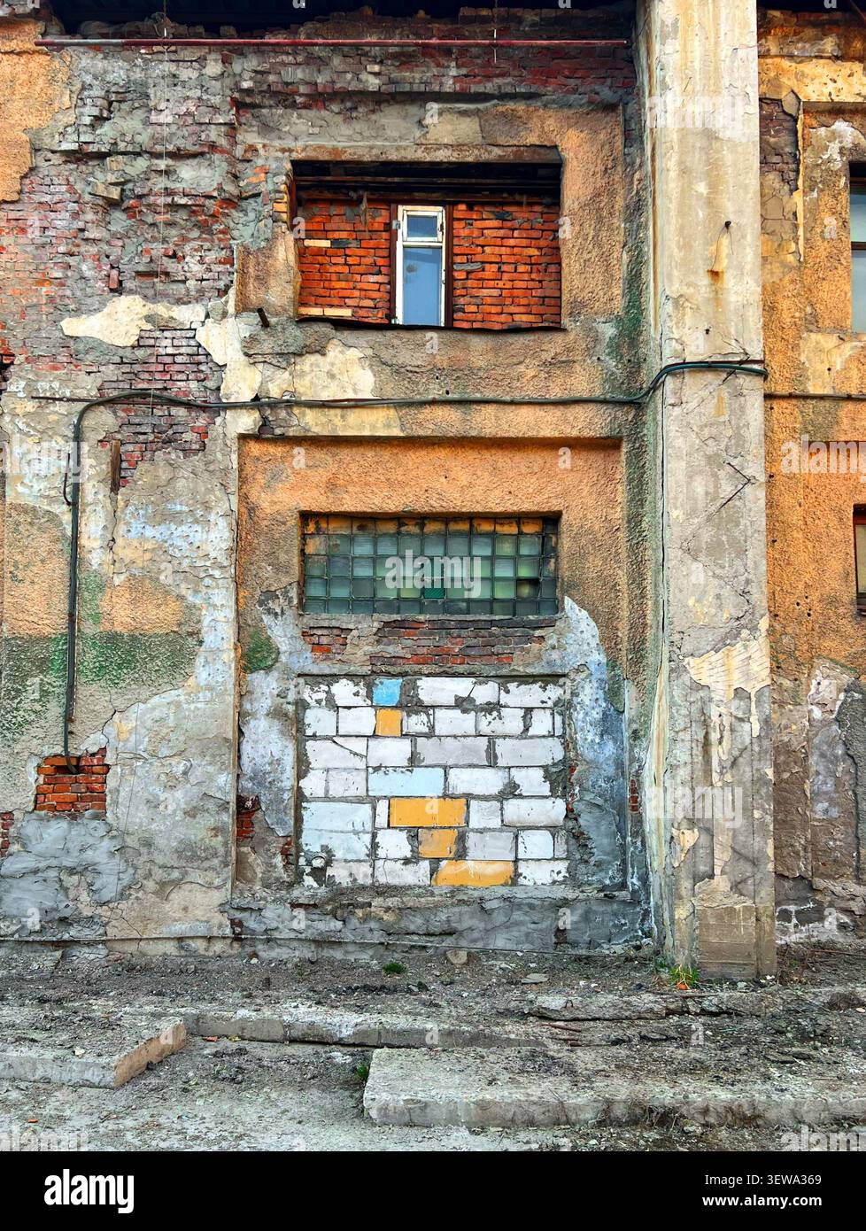 Façade en plâtre pelable d'un bâtiment industriel abandonné avec vieille fenêtre bloquée et brique apparente Banque D'Images