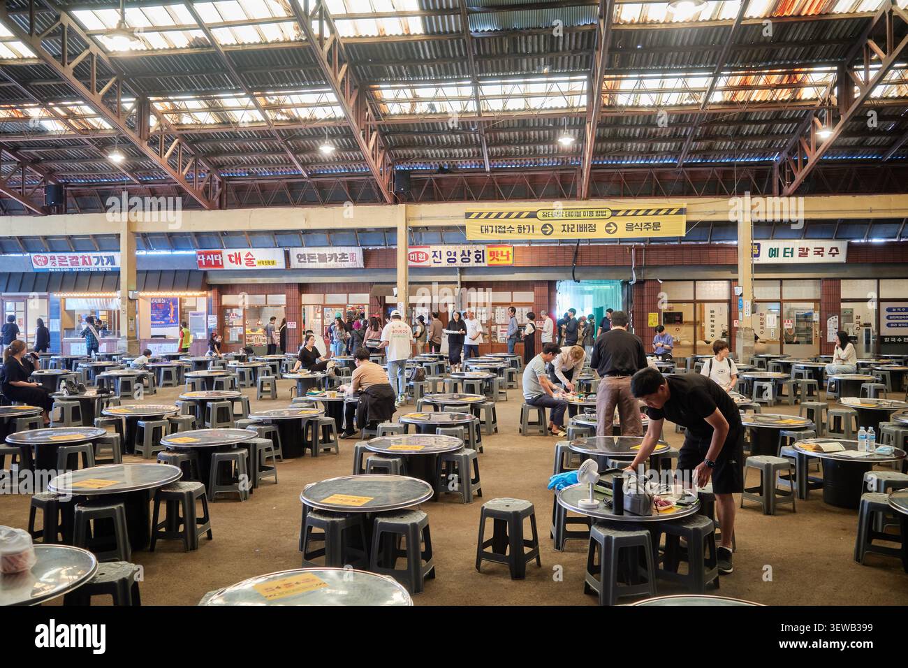 Vue panoramique sur une aire de restauration traditionnelle coréenne animée avec tables rondes et repas des visiteurs sous un grand toit métallique. Banque D'Images