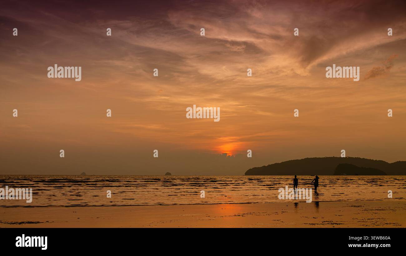 Couple aime se promener au coucher du soleil le long de la plage, créant de beaux souvenirs au bord de la rive. Banque D'Images