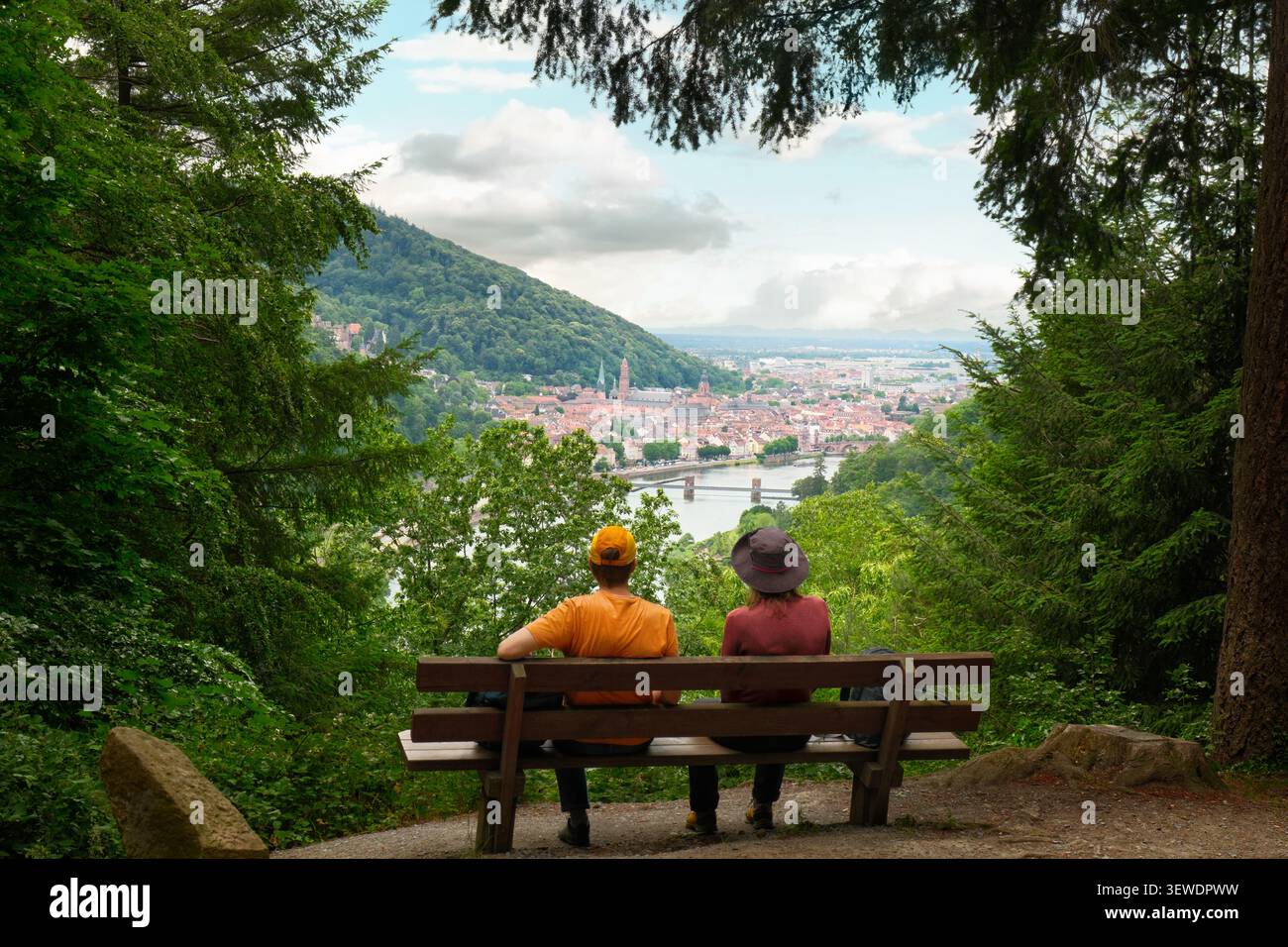 Remorquez des gens dans une forêt assis et relaxant sur un banc avec une vue spectaculaire sur la ville pittoresque de Heidelberg, en Allemagne. Banque D'Images