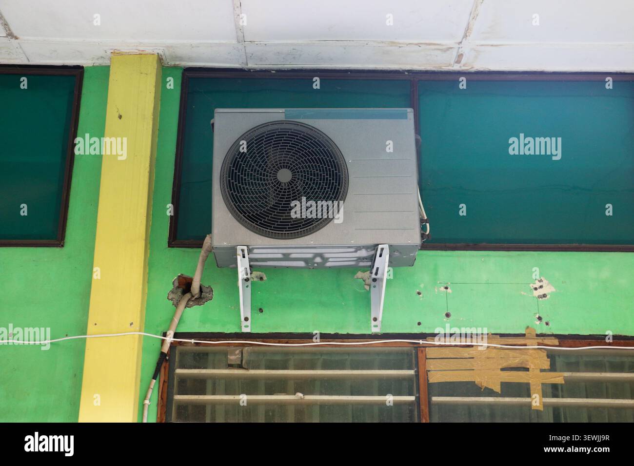 Unité de condenseur de climatiseur extérieur montée sur le mur du bâtiment avec ventilateur et support métallique Banque D'Images