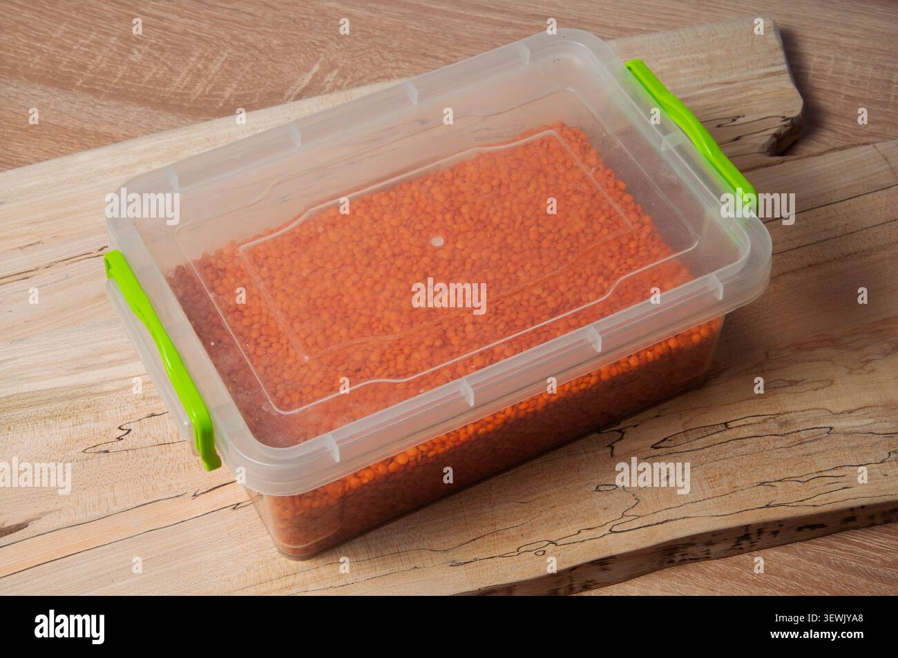 Lentilles rouges stockées dans un récipient en plastique transparent avec des fermoirs verts sur une surface en bois Banque D'Images