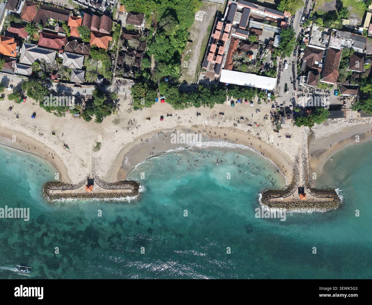 Vue aérienne de la plage de Sanur avec eau turquoise, côte sablonneuse, brise-lames en pierre et bâtiments environnants à Denpasar, Bali, Indonésie. Banque D'Images