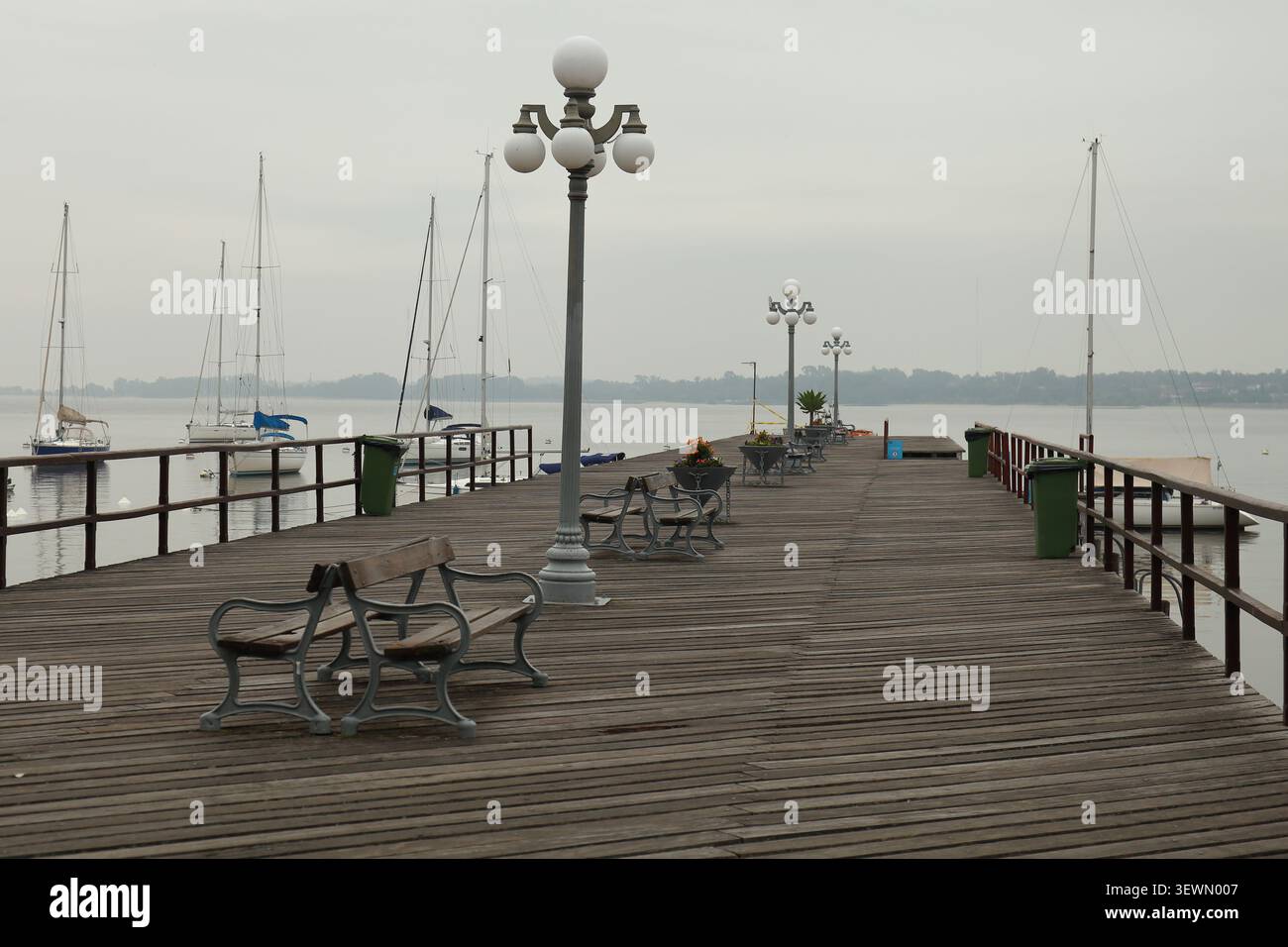 Jetée en bois avec lampadaires classiques, bancs et voiliers amarrés par une journée calme et nuageuse. Scène de front de mer photographiée à Colonia del Sacramento, U. Banque D'Images