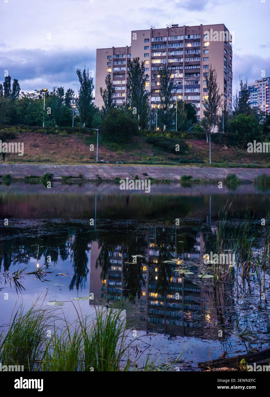 Immeuble résidentiel avec fenêtres éclairées reflétant dans l'eau calme du canal de la rivière Dnipro dans la ville de Kiev, paysage urbain au twil Banque D'Images