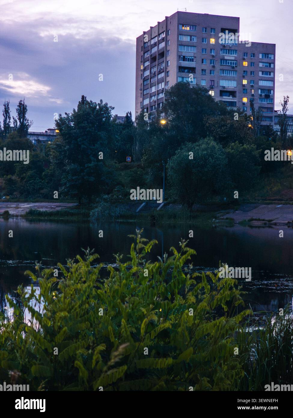 Bâtiment résidentiel urbain se dresse contre un ciel nuageux du soir, avec des lumières brillantes dans les fenêtres, donnant sur le canal de la rivière Dnipro dans la Rusanivka Banque D'Images