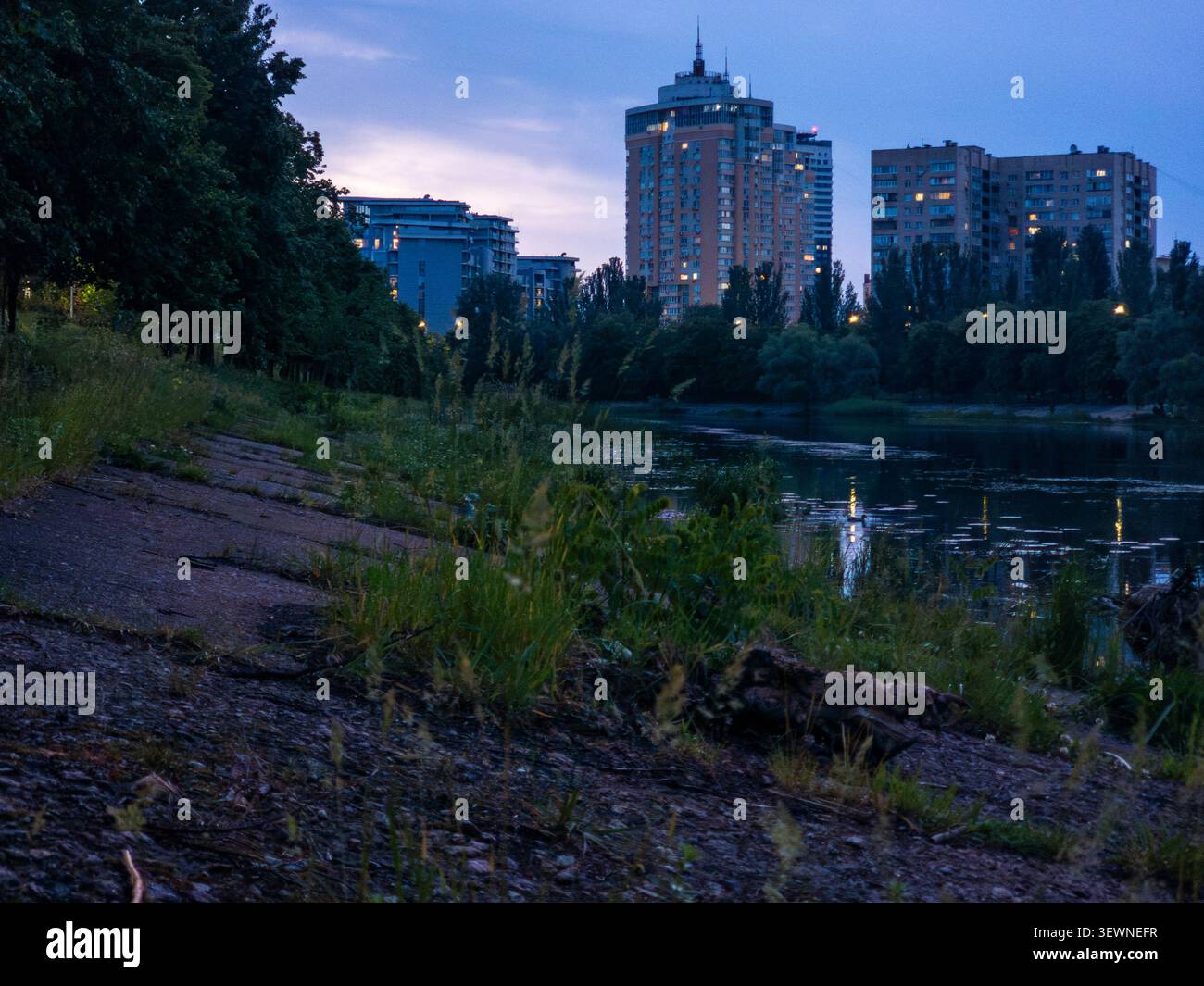 Les bâtiments de la zone résidentielle Rusanivka de Kiev illuminés au crépuscule, réfléchissant les lumières sur le paisible canal de la rivière Dnipro, créant une veille urbaine paisible Banque D'Images