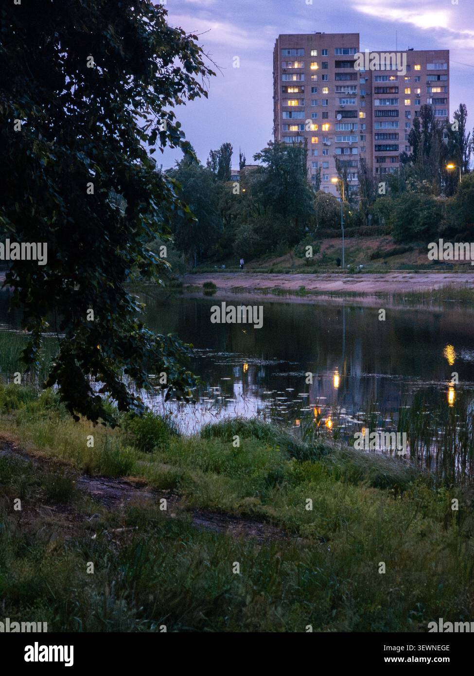 Rusanivka bâtiments résidentiels avec des fenêtres éclairées reflétant dans les eaux apaisantes du canal de la rivière Dnipro au crépuscule, entouré par l Banque D'Images