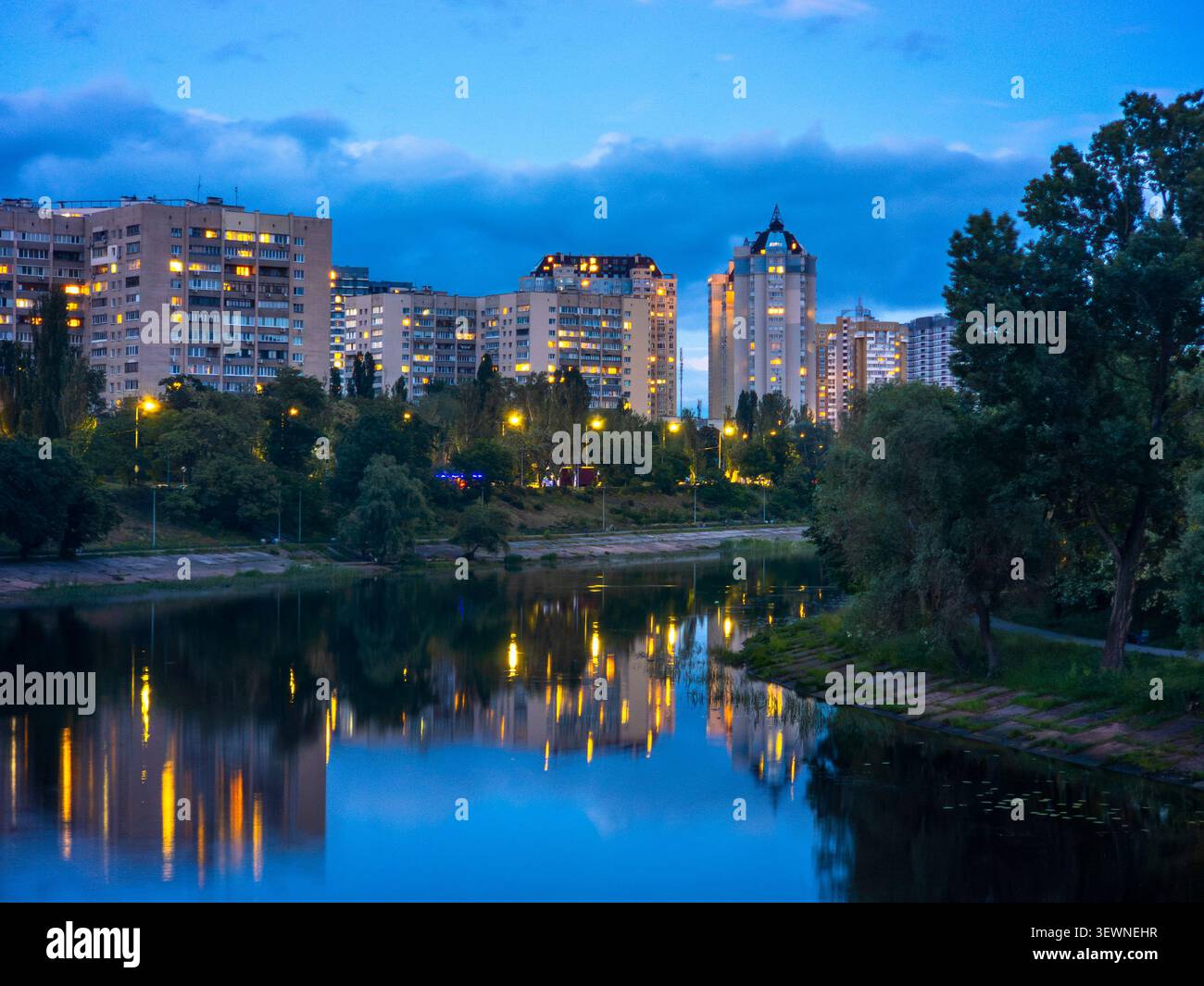Les bâtiments de la zone résidentielle de Rusanivka illuminent le ciel du soir, reflétant les lumières vibrantes sur le paisible canal de la rivière Dnipro, capturant la vie urbaine Banque D'Images