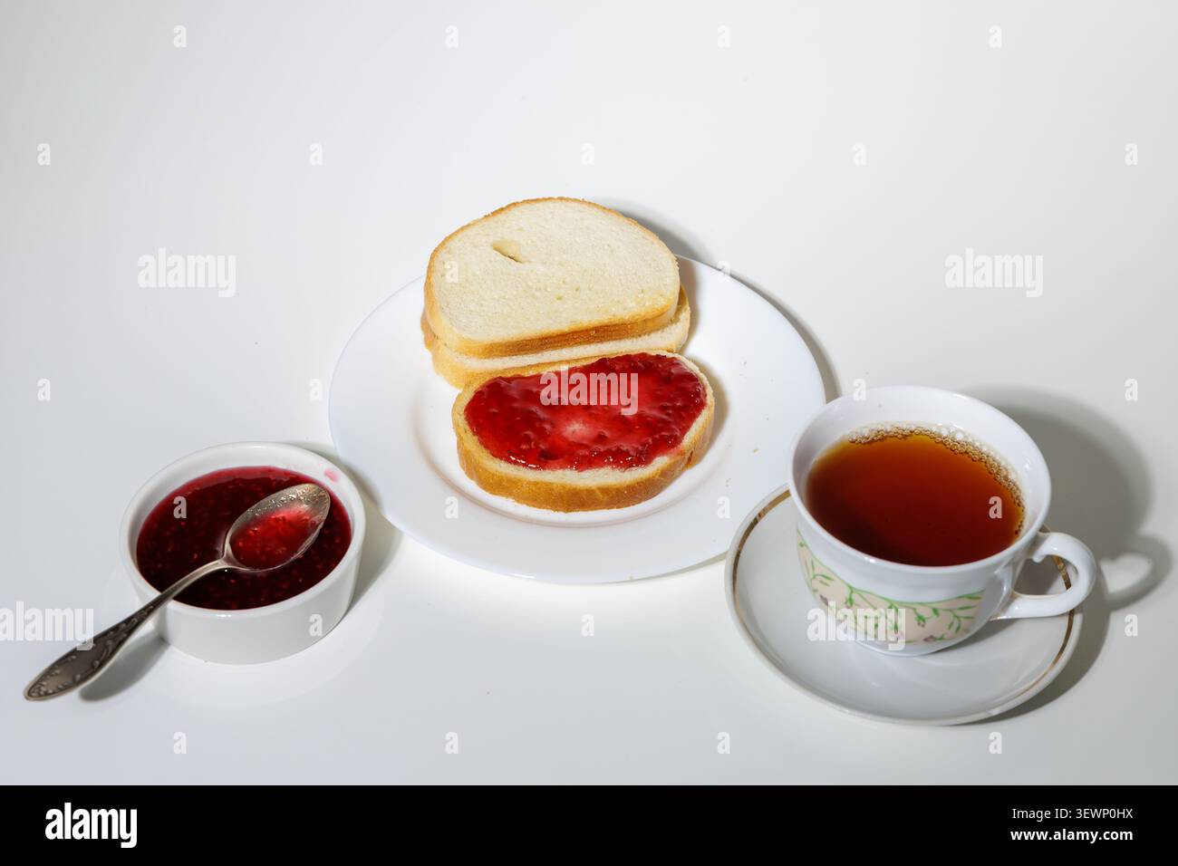 Pain ​​white fraîchement tranché à côté d'un pot de confiture de framboises. La confiture est rouge vif, avec des grains de baies distinctifs. Banque D'Images