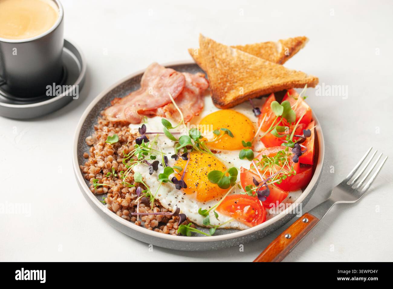 Petit déjeuner sain - œufs, pain grillé, sarrasin, bacon, haricots et tomates sur une assiette sur la table. Banque D'Images