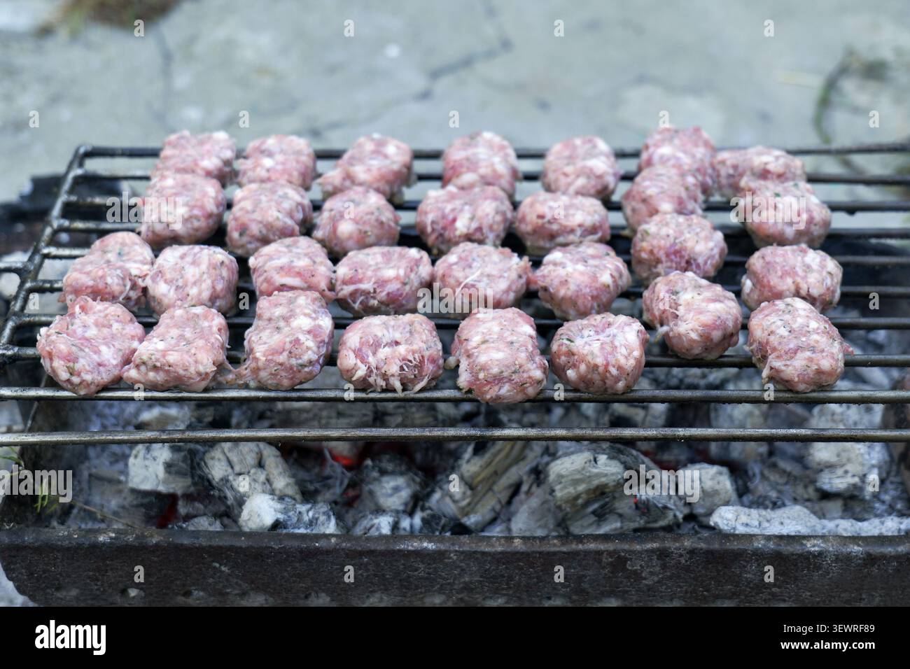 Boulettes de viande crues, traditionnellement connues sous le nom de MICI ou mititei, griller sur une grille métallique sur du charbon de bois chaud, préparer un repas en plein air Banque D'Images